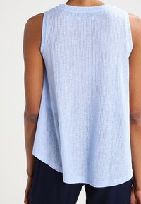 Canotta azzurro chiaro texturizzata senza maniche con una vestibilità ampia abbinata a pantaloni scuri, mostrata da dietro su una persona.