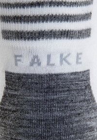 Grå och vita randiga strumpor i mjukt material, med ribbat mönster och märkesnamnet "FALKE" i ljusgrått nära toppen.