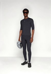 Ποδηλατική εμφάνιση που περιλαμβάνει ένα σκούρο γκρι, κοντομάνικο τζέρσεϊ και μαύροι σφιχτοί κολάν συμπίεσης, σε συνδυασμό με γκρι κράνος και μαύρα παπούτσια ποδηλασίας.