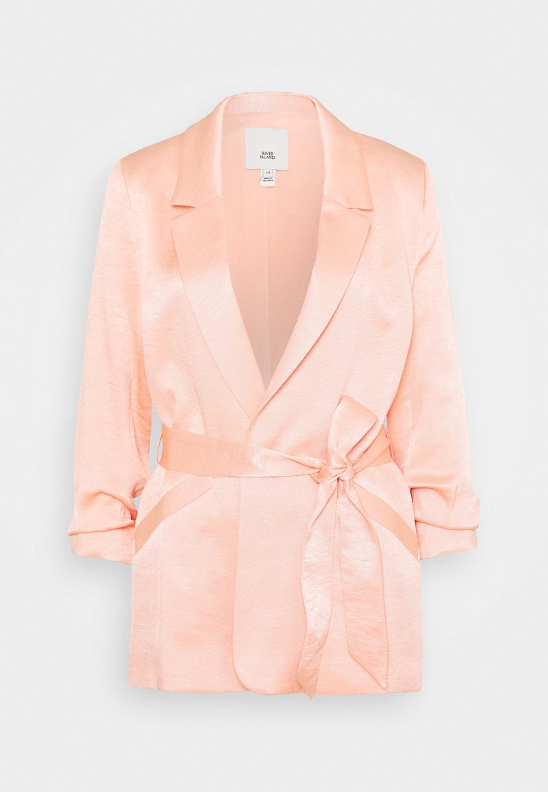 Blazer en satin rose clair avec larges revers, manches trois-quarts, poches latérales et ceinture nouée à la taille.