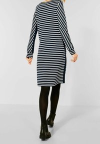 Långärmad klänning i marinblått och vitt med randigt mönster, med slitsar på sidan, mjukt tyg och rundad halsringning, matchad med svarta ankelboots och strumpbyxor.