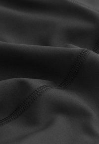 Gros plan sur un tissu noir avec une double rangée de coutures détaillées et une texture lisse, mettant en avant la précision de la couture et la qualité du matériau.