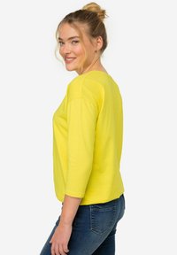 Gelbes Langarmshirt mit Rundhalsausschnitt und lockerem Schnitt, kombiniert mit dunkelblauen Jeans. Glatte Textur, keine sichtbaren Muster oder Akzente.