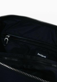 Svart dragkedjepåse med en slät nyloninteriör, dubbla fack och en logotag. Dragkedjans metallkomponenter är i silverfärg.
