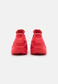 Ett par klarröda Adidas-sneakers visade bakifrån mot en vit bakgrund, med märkets trefoil-logga på hälarna.