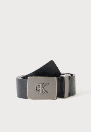 Ceinture en cuir noir texturé avec une boucle rectangulaire en argent ornée du logo en relief "cK" sur un fond blanc uni.