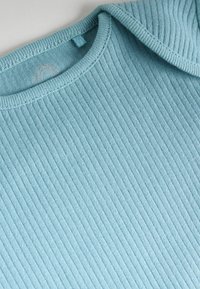 Rippiger, hellblauer Oberteil mit rundem Ausschnitt und kurzen Ärmeln. Weiche Textur mit nahtlosem Finish und minimalen Nähdetails.