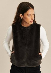 Nepbont vest in donkergrijs. Mouwloos ontwerp met een zachte textuur, voorzien van zijzakken en een ronde zoom. Gekocht over een witte longsleeve top.