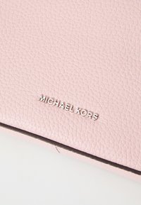 Rosa läderplånbok med texturerad yta, som har en silverfärgad "MICHAEL KORS"-logotyp och svart kant längs kanterna.