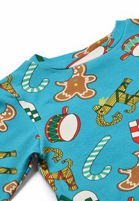 Mėlyna medvilninė marškinė su pakartojančiu imbierinių vyrų, saldžiųjų lazdelės, būgnų ir šventinių akcentų raštu. Minkšta tekstūra su apvalia kaklo iškirpte.