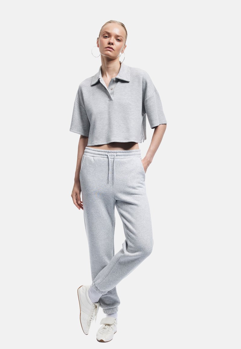 Grå kortærmet polo shirt i en cropped stil, parret med grå sweatpants. Inkluderer elastisk talje og manchetter. Hvide sneakers fuldender looket.