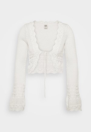 Cardigan blanc court avec une texture tricotée, des bords festonnés, de longues manches évasées et un cordon de serrage à l'avant.
