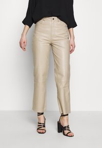 Beiga läderbyxor med hög midja, raka ben och kort längd, i kombination med svarta strappy högklackade sandaler.