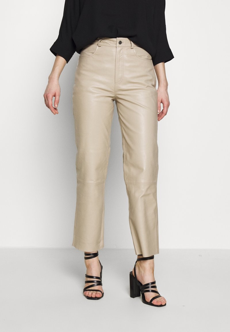 Beiga läderbyxor med hög midja, raka ben och kort längd, i kombination med svarta strappy högklackade sandaler.