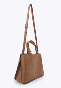 Sac à main en daim brun avec une forme structurée, deux poignées courtes et une sangle longue ajustable, devant un fond blanc.