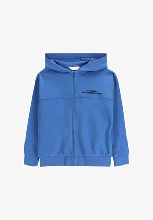 Niebieska bluza z kapturem zapinana na zamek, z przednimi kieszeniami i czarnym napisem na lewej piersi: „TO NIE WANDALIZM, TYLKO AGRESYWNE DEKOROWANIE.”