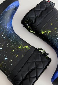 Bottes de pluie en caoutchouc noires avec un motif galactique en bleu et vert néon. Poignet en tissu matelassé avec cordon de serrage, offrant isolation et style.