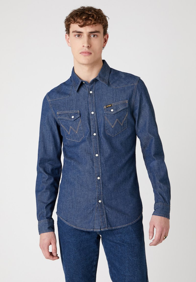 Blauwe denim overhemd met puntkraag, knoopsluiting, twee borstzakken, vervaagde stiksels en lange mouwen, gedragen met bijpassende denim broek.
