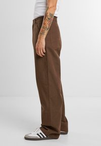 Braune Baumwollhosen mit geradem Schnitt, ausgestattet mit Gesäßtaschen und umgeschlagenem Saum, kombiniert mit weißen, grauen und schwarzen Sportschuhen.