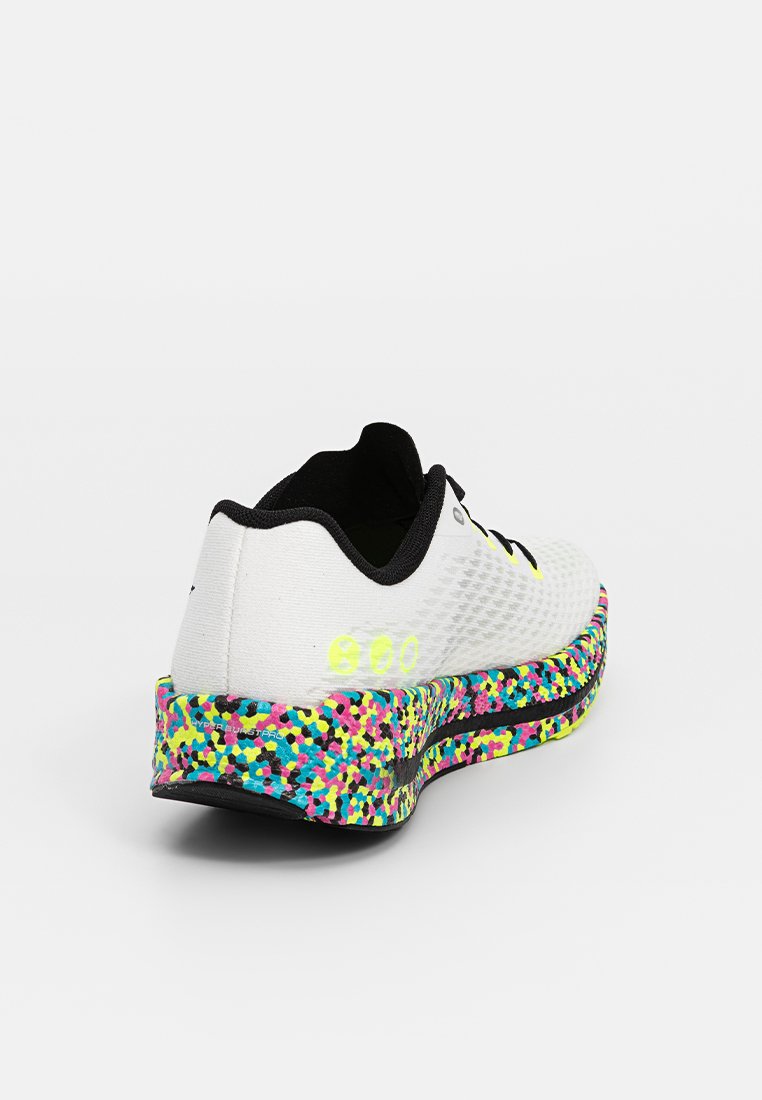Botte de sport blanche avec une tige texturée, des accents noirs et une semelle multicolore à motifs tachetés de rose, jaune et bleu canard.
