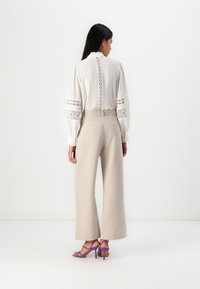 White blouse with lace inserts and puff sleeves paired with high-waisted beige wide-leg trousers and purple strappy heels.