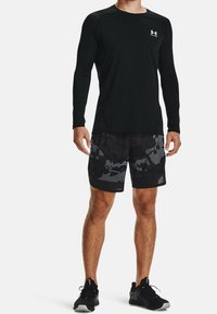 Svart långärmad t-shirt i sportmodell kombinerad med svarta kamouflageshorts och svarta sportskor; stilren design med fukttransporterande material.