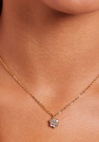 Gouden ketting met een bloemenhanger waaraan meerdere kleine, heldere stenen zijn bevestig in de vorm van een bloem. Glad, glanzend oppervlak.