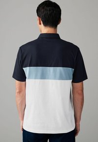 Lühikeste varrukatega polo särk, millel on tumesinine ülaosa, helesinine tekstuuriga paneel ja valge alumine osa. Klassikaline krae ja sirge äär.