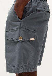 Pantaloni scurți gri dintr-un material ușor, având o buzunar lateral cu închidere buton și un mic eticheta a mărcii. Design simplu, croială lejeră.