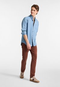 Lichtblauw overhemd met lange mouwen en knopen in bruin, gecombineerd met bruine slim-fit broek en beige sneakers met suède en leren accenten.