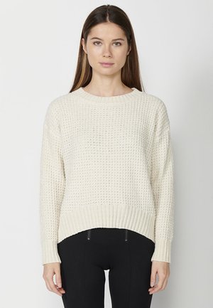 Pull en maille crème clair avec un motif texturé, poignets et ourlet côtelés. Encolure ronde et dos légèrement plus long. Coupe décontractée.