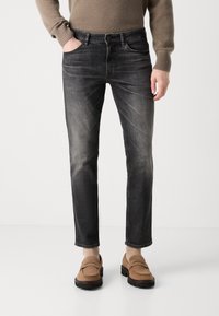 Blugi negri din denim cu o tăietură slim și spălare uzată, având buzunare frontale și închidere cu nasture, asociați cu mocasini maro.