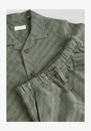 Set de cămașă și pantaloni texturat de culoare verde deschis. Cămașa are guler și nasturi maro, iar pantalonii au un tiv elastic și o textură asemănătoare.