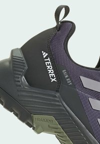 Mörklila träningssko med överdel av mesh, gummisulor, greppdetaljer och Terrex-logotyp i vitt. Förstärkt häl för stöd.