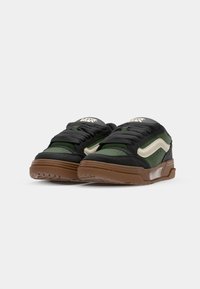 Sort og grøn sneaker med en tekstureret finish, der har et hvidt swoosh, brun sål og polstret tungespids, designet til komfort og stil.