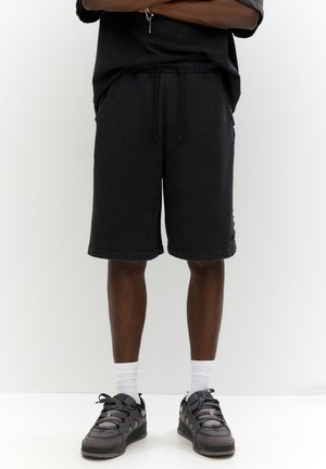 Sorte bomuldsshorts med elastisk talje og snøre; knælange med sidelommer; båret med grå sneakers og hvide sokker.