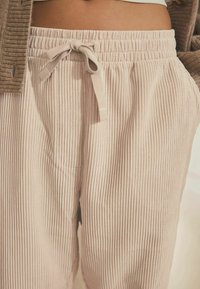 Heledad beez maakardid püksid ribakujulise tekstuuriga, elastse vöökoha ja esi side detailiga, millel on nurga all asuvad küljetaskud.