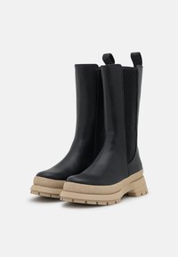 Czarne botki z elastycznymi bokami, wykonane ze skóry gładkiej, z masywną beżową gumową podeszwą i teksturowanymi detalami na podeszwie.