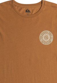 Brown cotton t-shirt featuring a round neck and a circular logo with text on the left chest. Soft texture and casual fit.