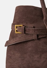 Hnědá semišová kabelka s texturovaným povrchem, vybavená zlatou obdélníkovou sponou a páskem obtočeným kolem vršku.