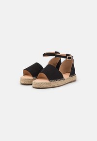 Černé semišové espadrilky s otevřenou špičkou, kotníkovým páskem a tkanou juteovou podrážkou. Mají plochý podpatek a hladký vnitřek.