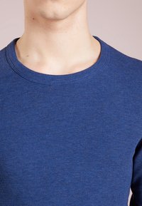 Blå stickad tröja med rund halsringning. Texturen är ribbad, gjord av ett mjukt material, vilket ger en åtsittande look utan ytterligare detaljer.