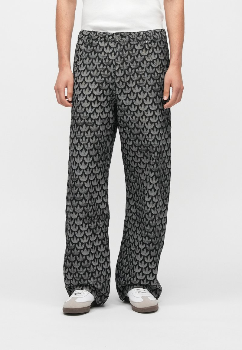 Melnas un pelēkas rakstaina platām kājām bikses ar atkārtotu lapu motīvu un elastīgu jostasvietu. Valkātas ar baltām sporta kurpēm.