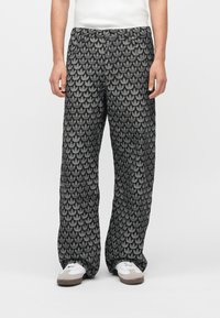 Juodos ir pilkos spalvų raštuotos plačios kojų kelnės su pasikartojančiu lapų motyvu ir elastine juosmens juosta. Dėvimos su baltais sportbačiais.