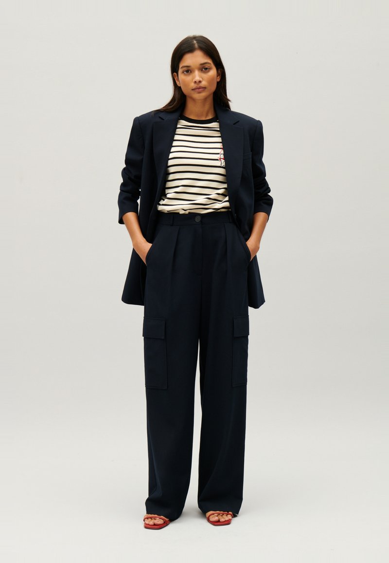 Marynarski, dopasowany blezer na paski z podkoszulkiem i szerokimi spodniami cargo. Posiada duże kieszenie i luźny krój. Sandały z płaską podeszwą.