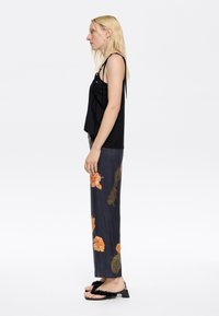 Black sleeveless top, gray floral long skirt with orange flowers, and black sandals with fuzzy texture. Side profile view.