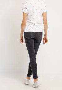 Vit kortärmad skjorta med rosa saxmönster, kombinerad med åtsittande grå jeans och vita sneakers, sedd bakifrån.