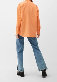 Orange bomulds skjorte med lange ærmer, knappede manchetter og afslappet pasform, parret med lyseblå højtaljede jeans og sorte platform sko.
