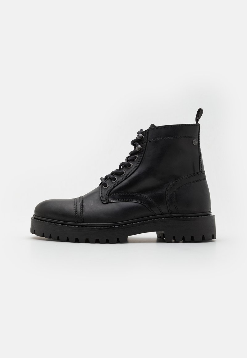 Botas de cuero negro hasta el tobillo con punta redonda, diseño de cordones, suela robusta y detalles de costura. Presenta una asa en el cuello.