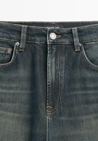 Jeans in denim blu scuro con tasche frontali visibili, passanti per cintura, chiusura con bottone in metallo e etichetta "Massimo Dutti" all'interno della cintura.